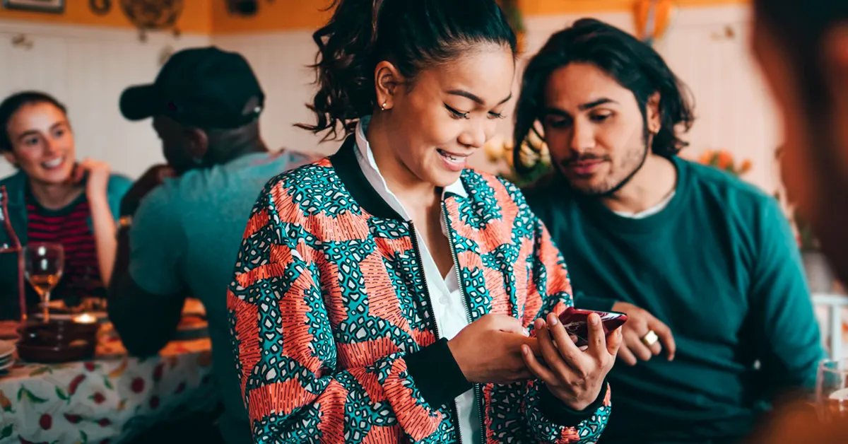 Smiling young woman sharing smart phone with male friend while sitting at restaurant
